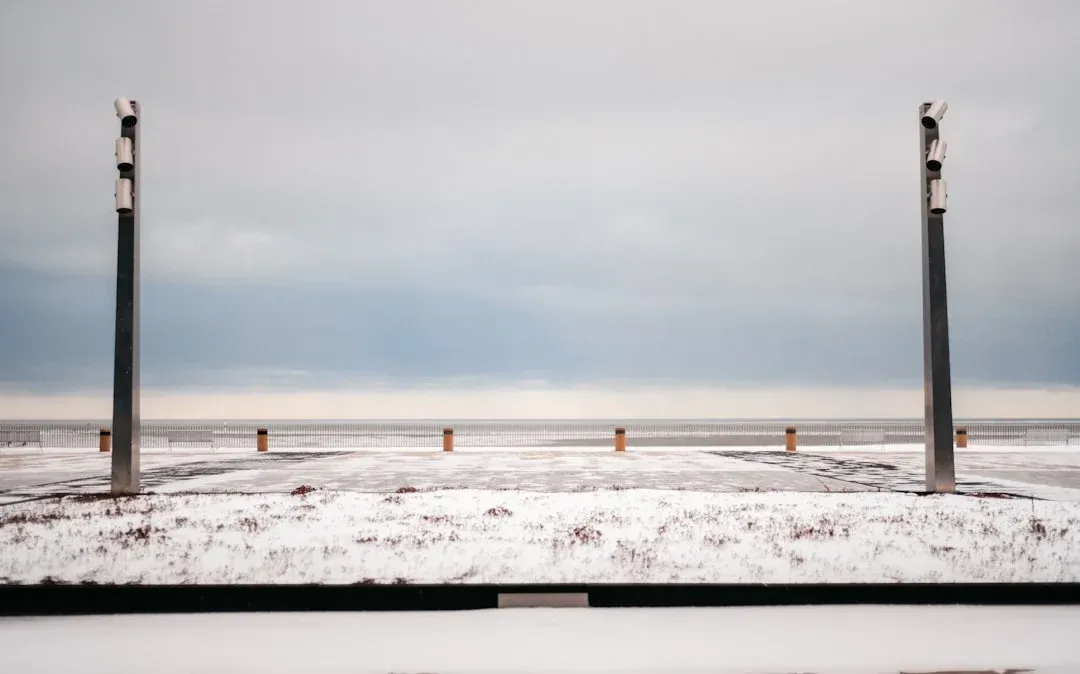 Frozen metal raised garden bed with frost-covered soil and snow, flanked by two tall dark posts under overcast winter sky.